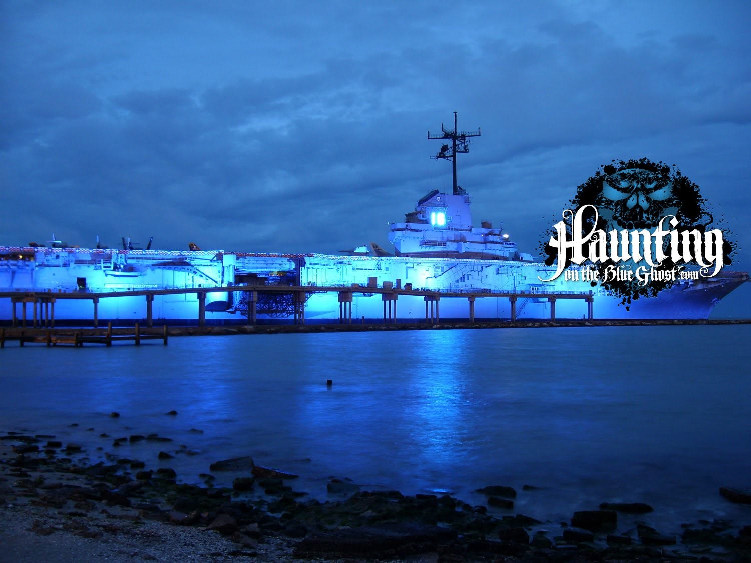 USS Lexington illuminated in blue at dusk, with the Haunting on the Blue Ghost logo